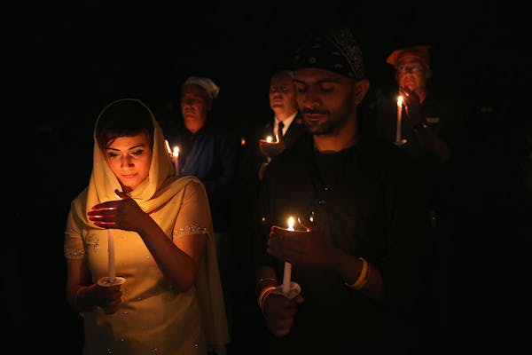 A woman's face is illuminated by the candle she holds, and she and a man beside her stand in a crowd at night.