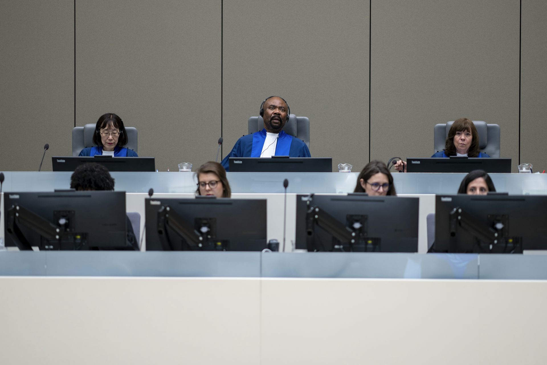 Three judges in blue robes sit in a row behind people looking at computer screens.