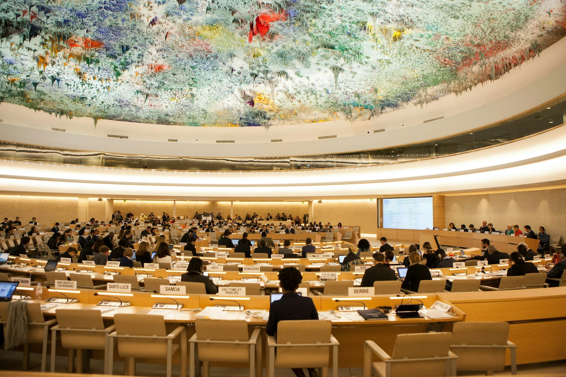 People in an ornate meeting hall with a colourful ceiling.