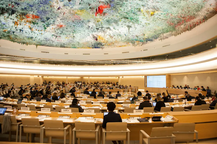 People in an ornate meeting hall with a colourful ceiling.