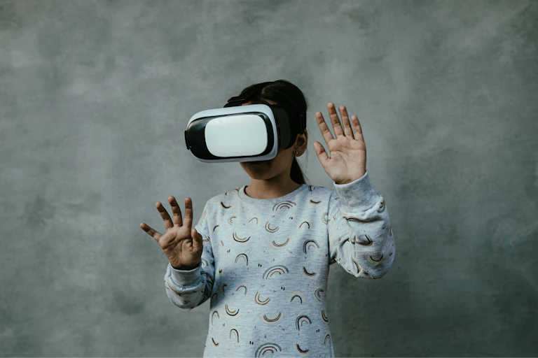 a child wearing VR goggles with her hands raised in front of her