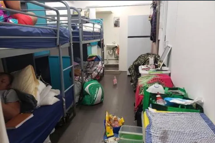 A room with two bunk beds next to each other and a floor filled with personal belongings