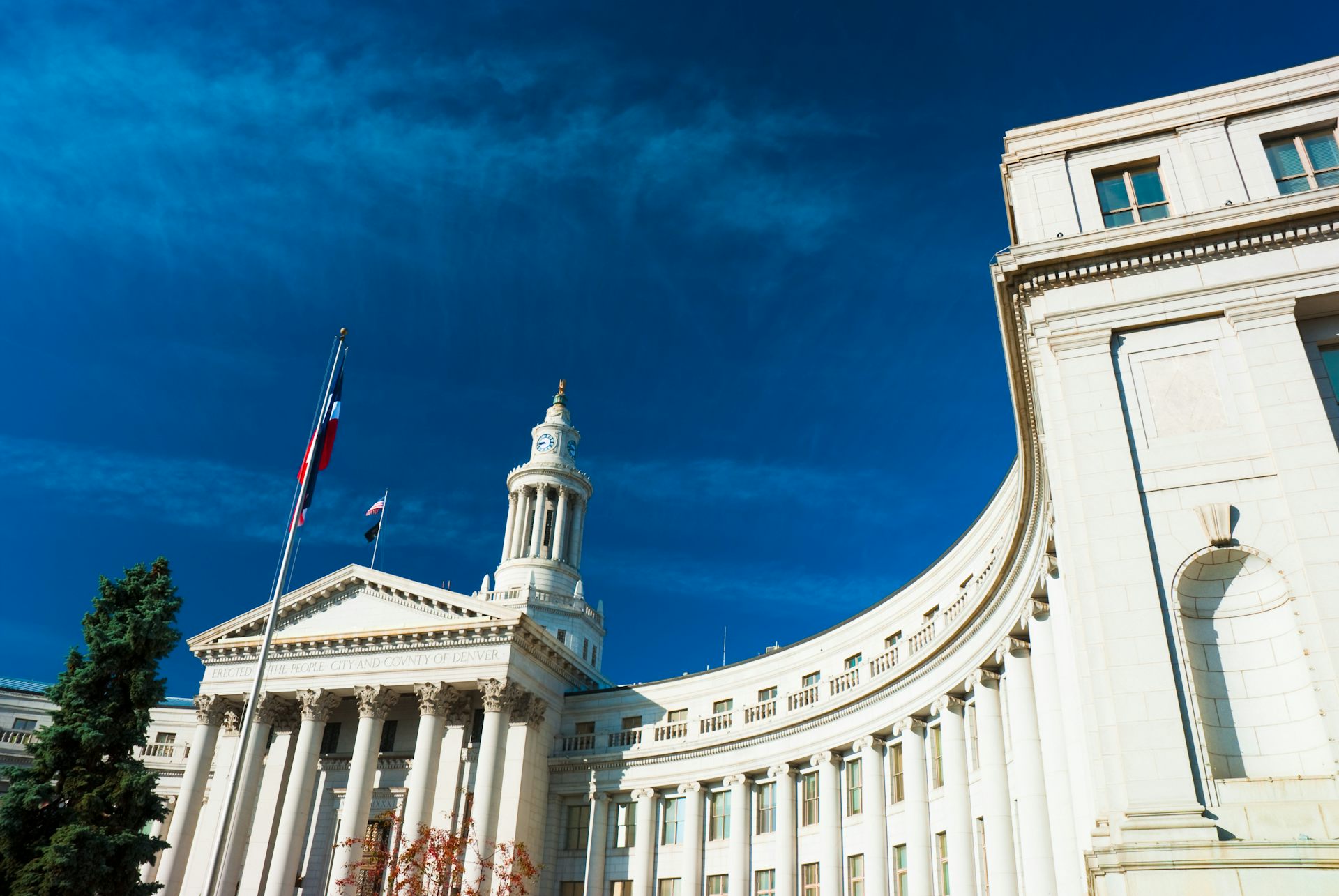 A formal-looking official curved white building with columns and a golden spire.