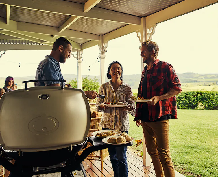 people standing around a gas barbeque having a good time.