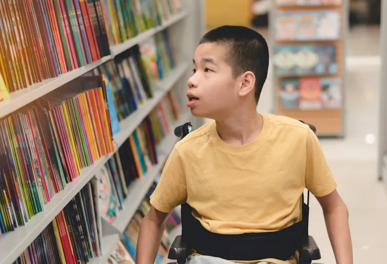 Boy in wheelchair looking at titles in library