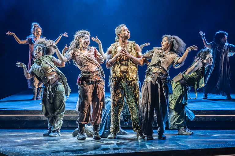 A theatre troup of mainly women surrounding a man on stage, arms aloft
