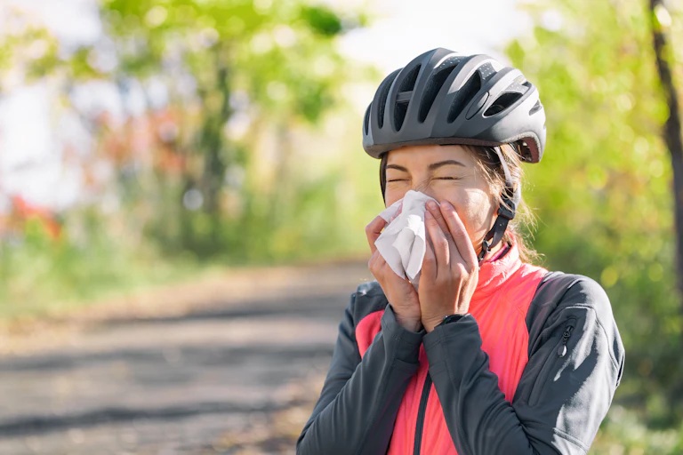 A woman wearing a bicycle helmet blows her nose into a tissue.