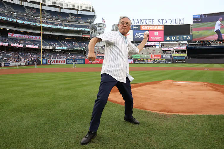 A man in his early 80s wearing Yankees gear gears up to throw a ball at Yankee Stadium.