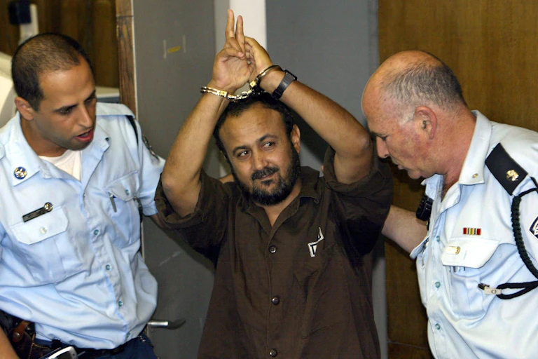 Palestinian activist Marwan Barghouti holds his handcuffed arms over his head as he is led into court by two Israeli guards.