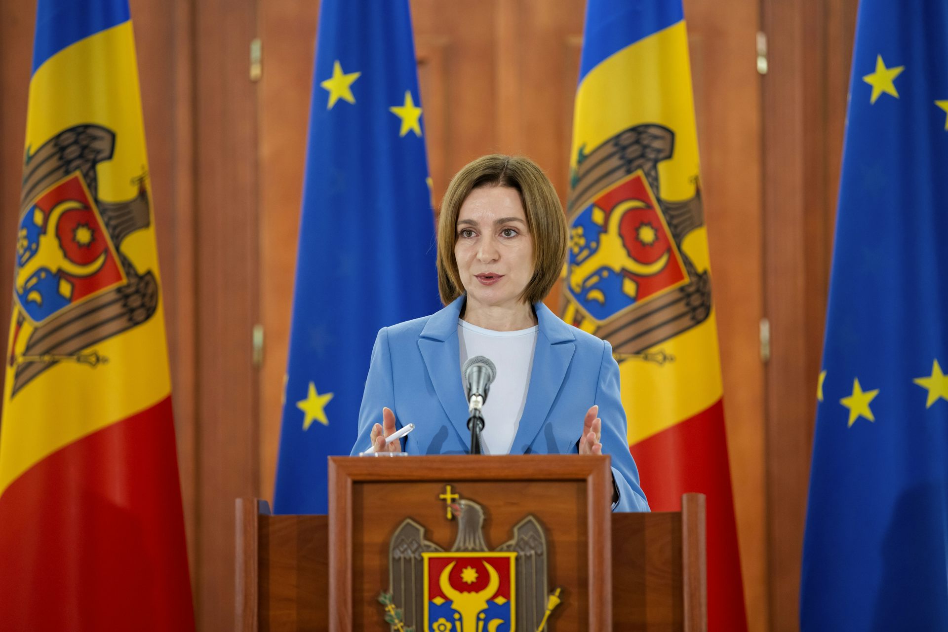 Moldovan president, Maia Sandu, stands at a podium in front of Moldovan and EU flags.