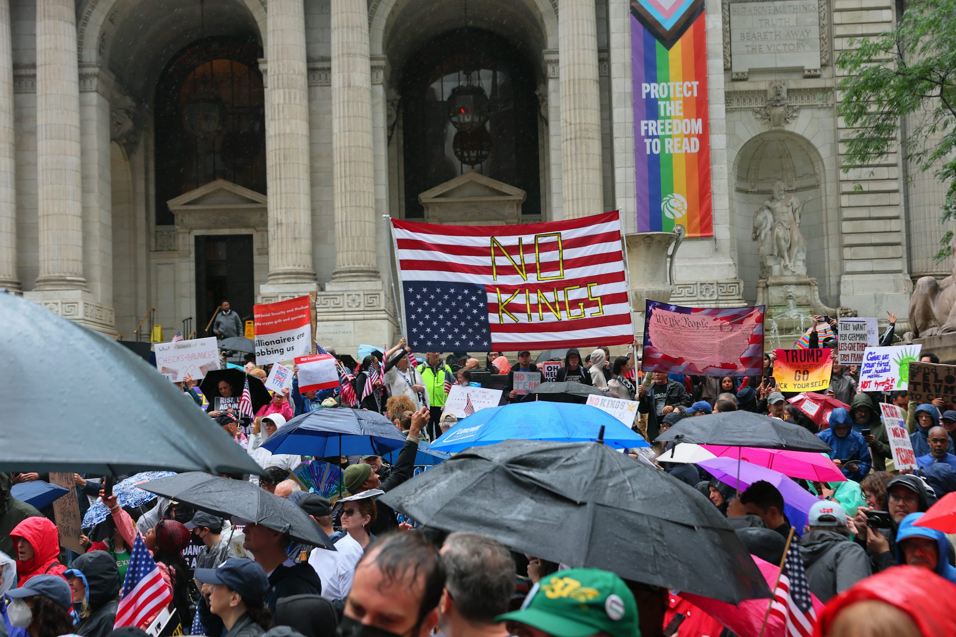 A crowd before the steps of a large building, carrying signs and an upside-down American flag.