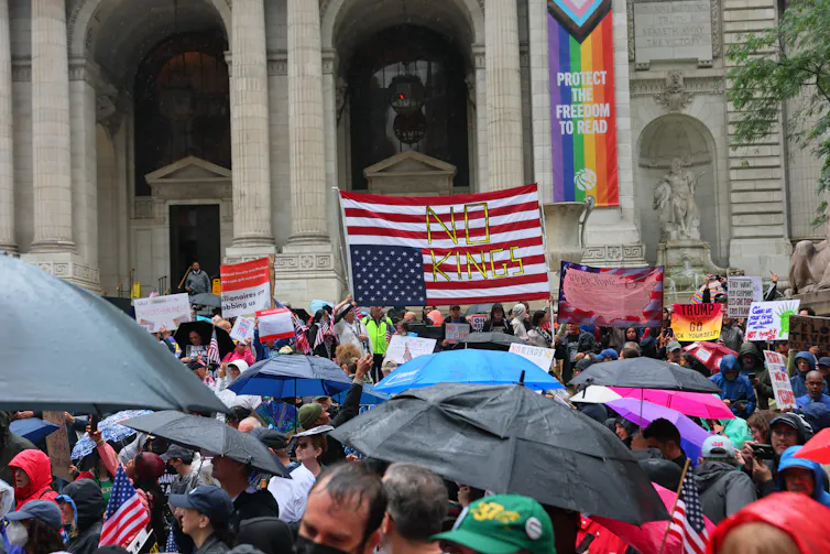 A crowd before the steps of a large building, carrying signs and an upside-down American flag.