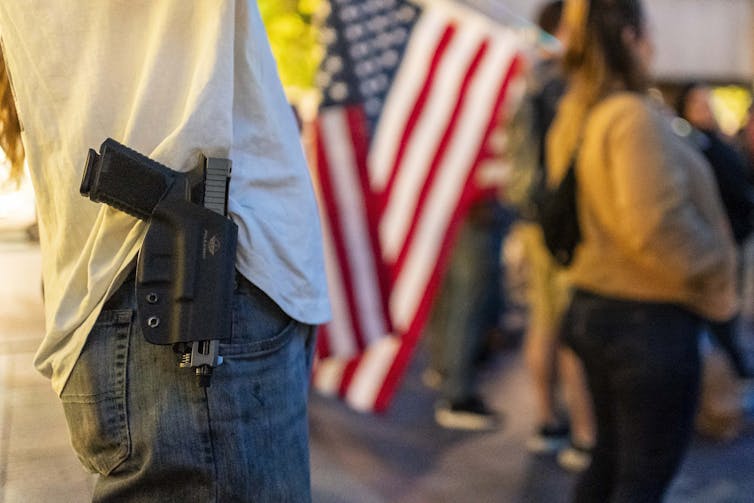 An attendee wears a gun on their hip during a candlelight vigil and prayer event at which an American flag is displayed.