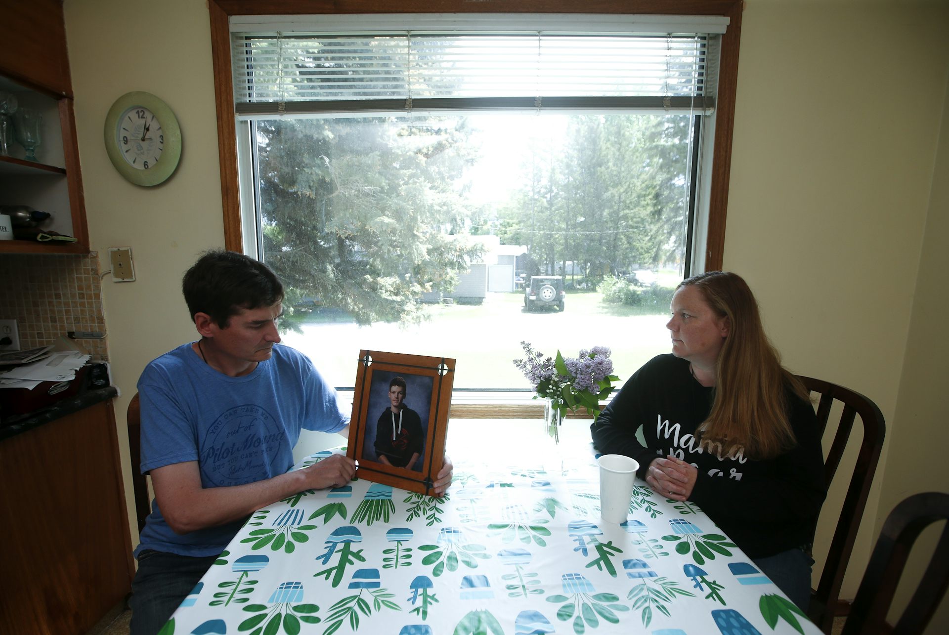 Dos padres se sientan en una mesa de cocina, un padre que sostiene una foto de un adolescente
