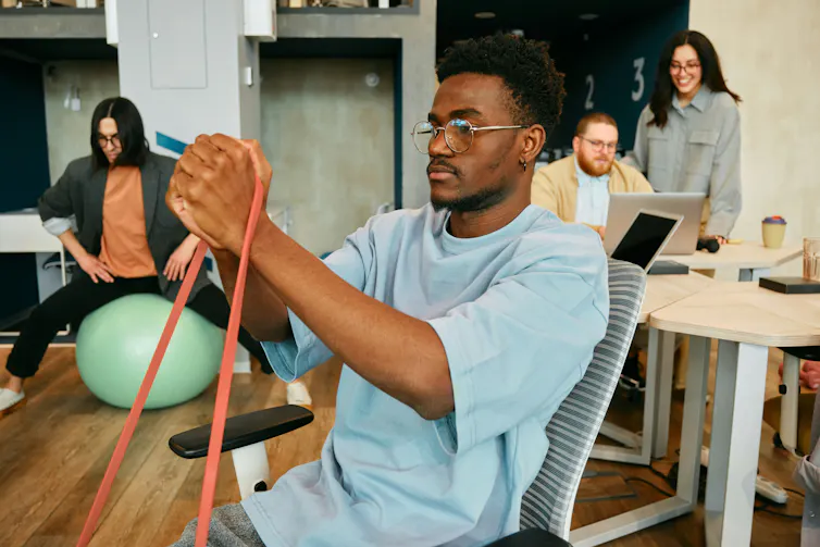 Des personnes dans un bureau, dont l’une est assise sur un ballon d’équilibre et l’autre utilise une bande d’exercice pour renforcer ses bras