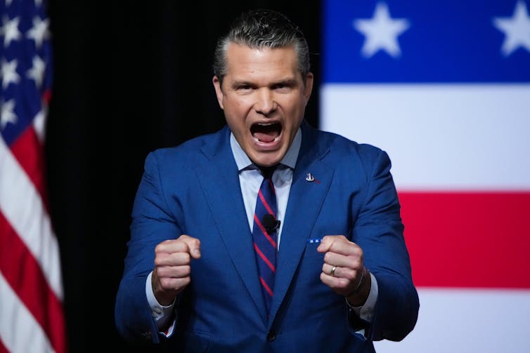 El hombre frente a la bandera de los Estados Unidos, parece estar gritando y extendiendo su puño.