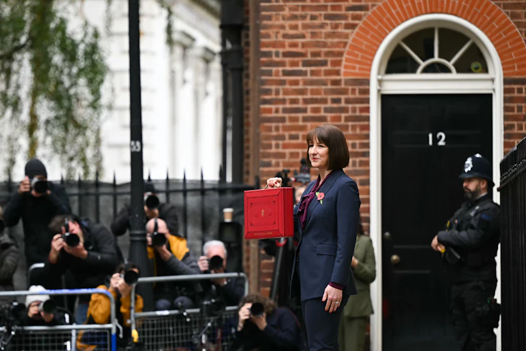 A women holds a red briefcase outside a brick building.