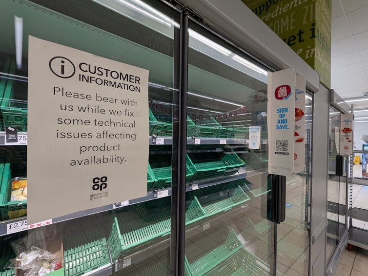 Empty shelves in a co-op store behind a sign explaining that the chain is working through some technical challenges.