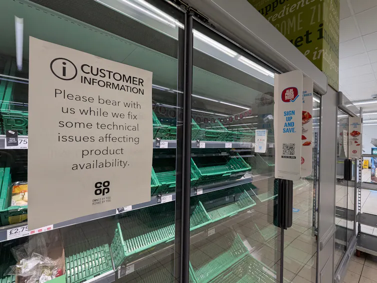 Empty shelves in a co-op store behind a sign explaining that the chain is working through some technical challenges.