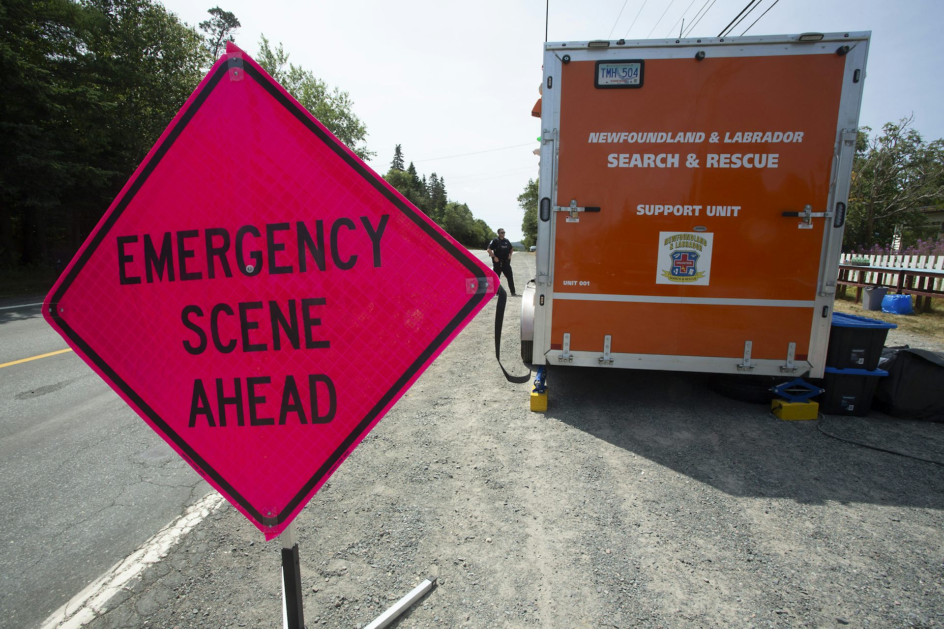 Un gran letrero de diamante rojo que dice la situación de emergencia frente al plano frontal con un camión de búsqueda naranja y rescate detrás