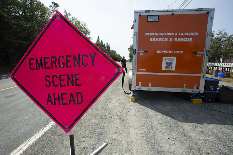 Un gran letrero de diamante rojo que dice la situación de emergencia frente al plano frontal con un camión de búsqueda naranja y rescate detrás