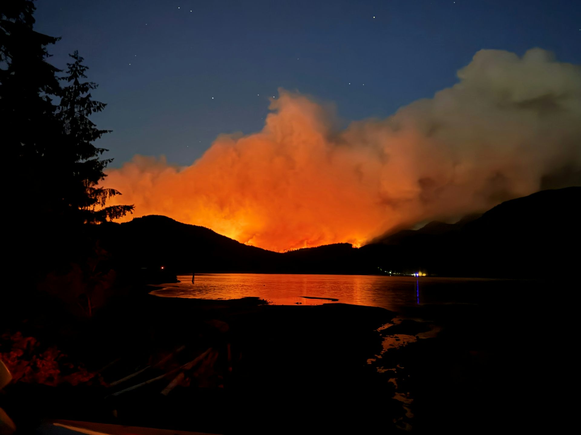 A lake and mountains with orange flame and smoke on the horizon