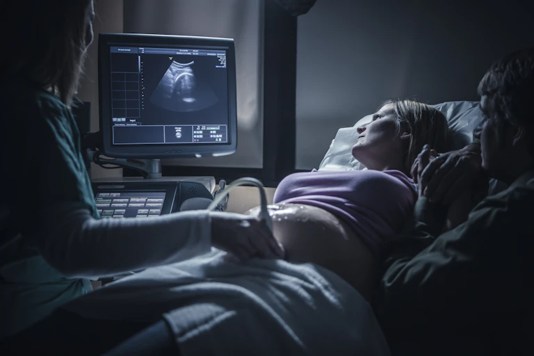 Woman lying on her back as doctor performs a sonogram, with both patient and partner staring at the screen.