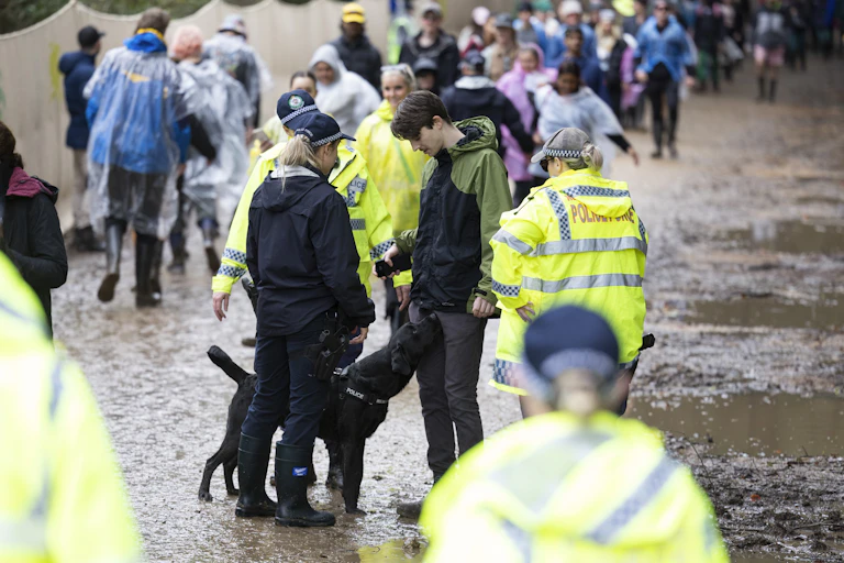 Three police officers and a dog stop a young man at a musical festival