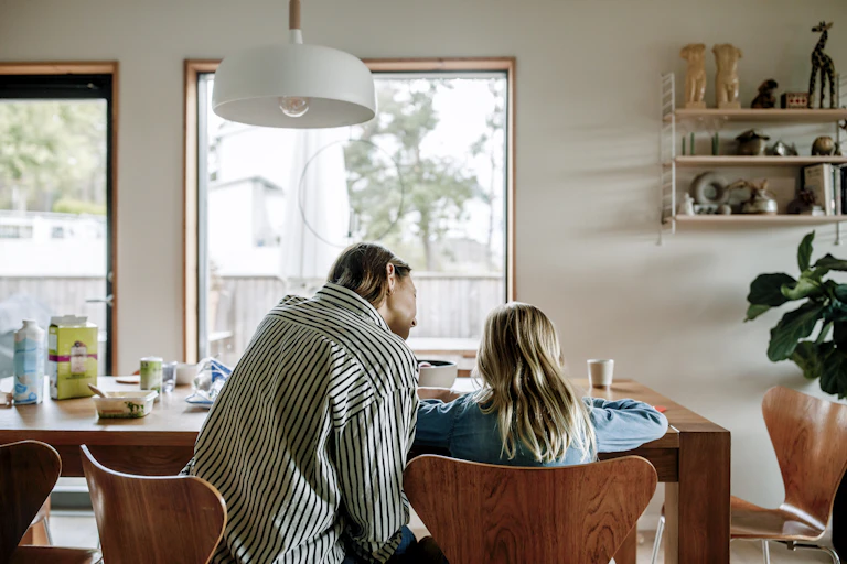 A rear view of a woman sitting next to a child at a desk.