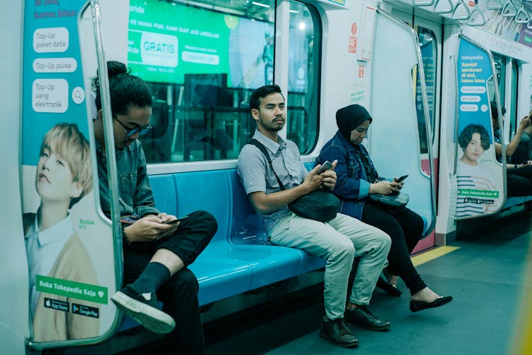 three people sitting on a train with their mobile phones in hand
