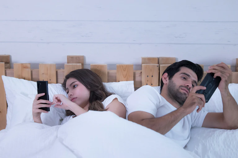 a couple in bed on their phones facing away from each other