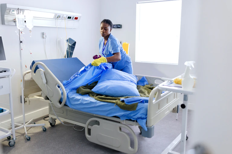 Cleaner pulls bedsheets off hospital bed.