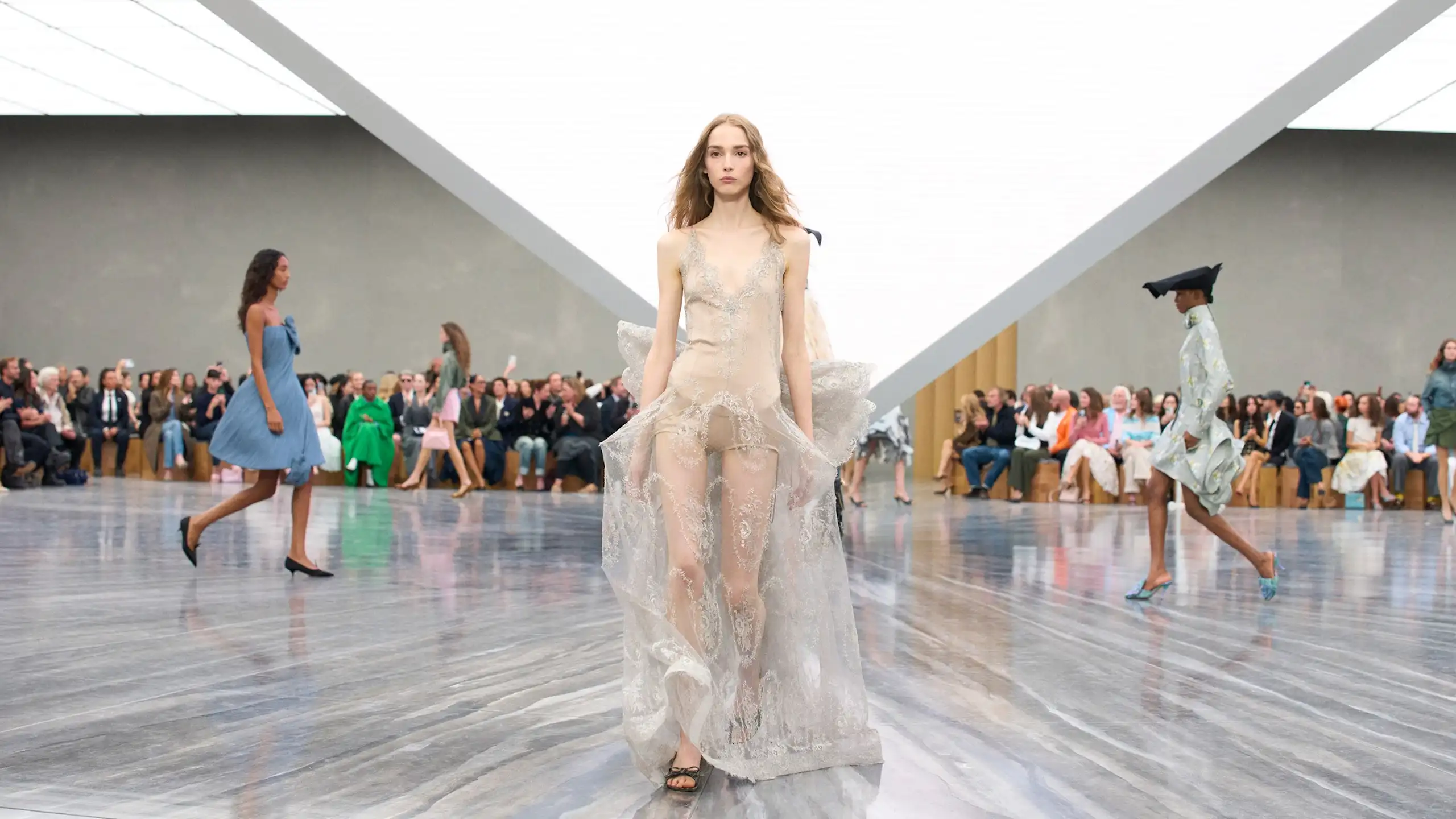 Una modelo desfila con un vestido claro en una sala muy iluminada.