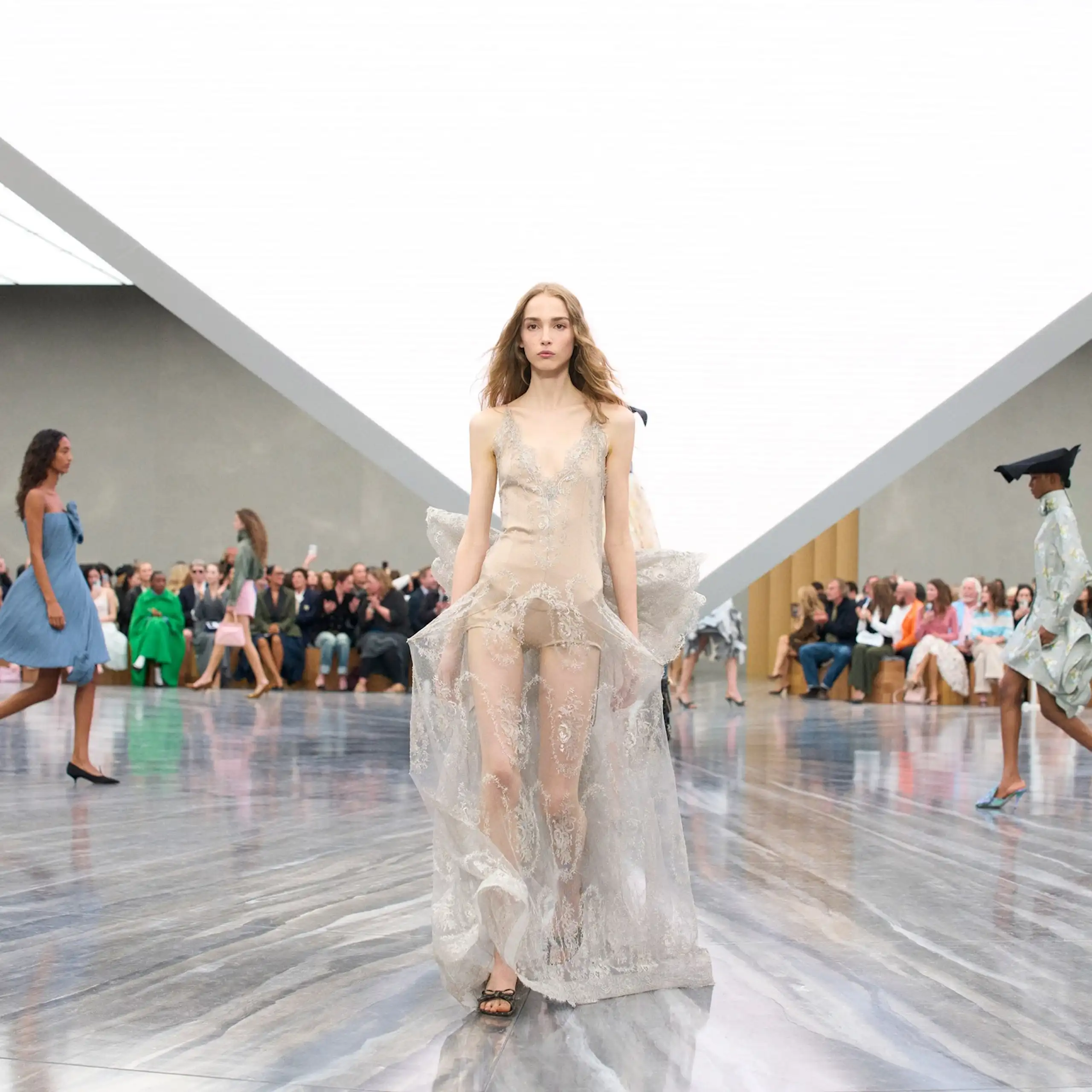 Una modelo desfila con un vestido claro en una sala muy iluminada.