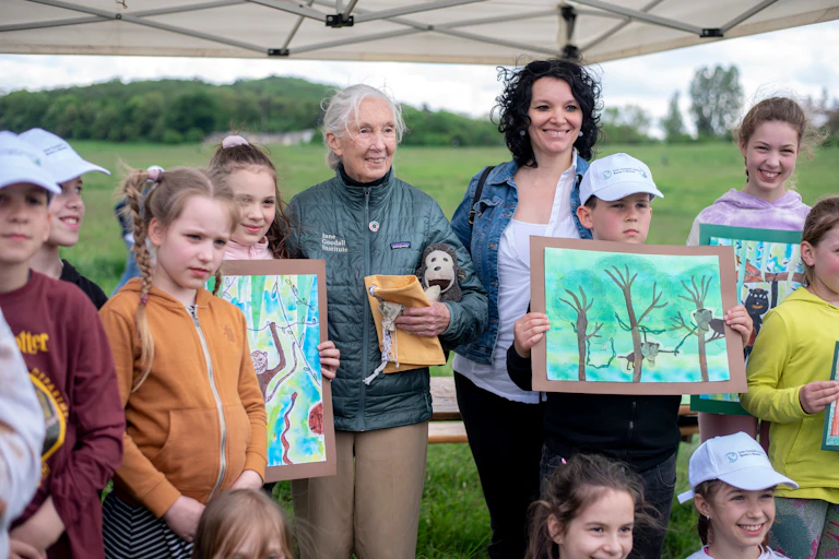 Una mujer rodeada de niños que sostienen dibujos.