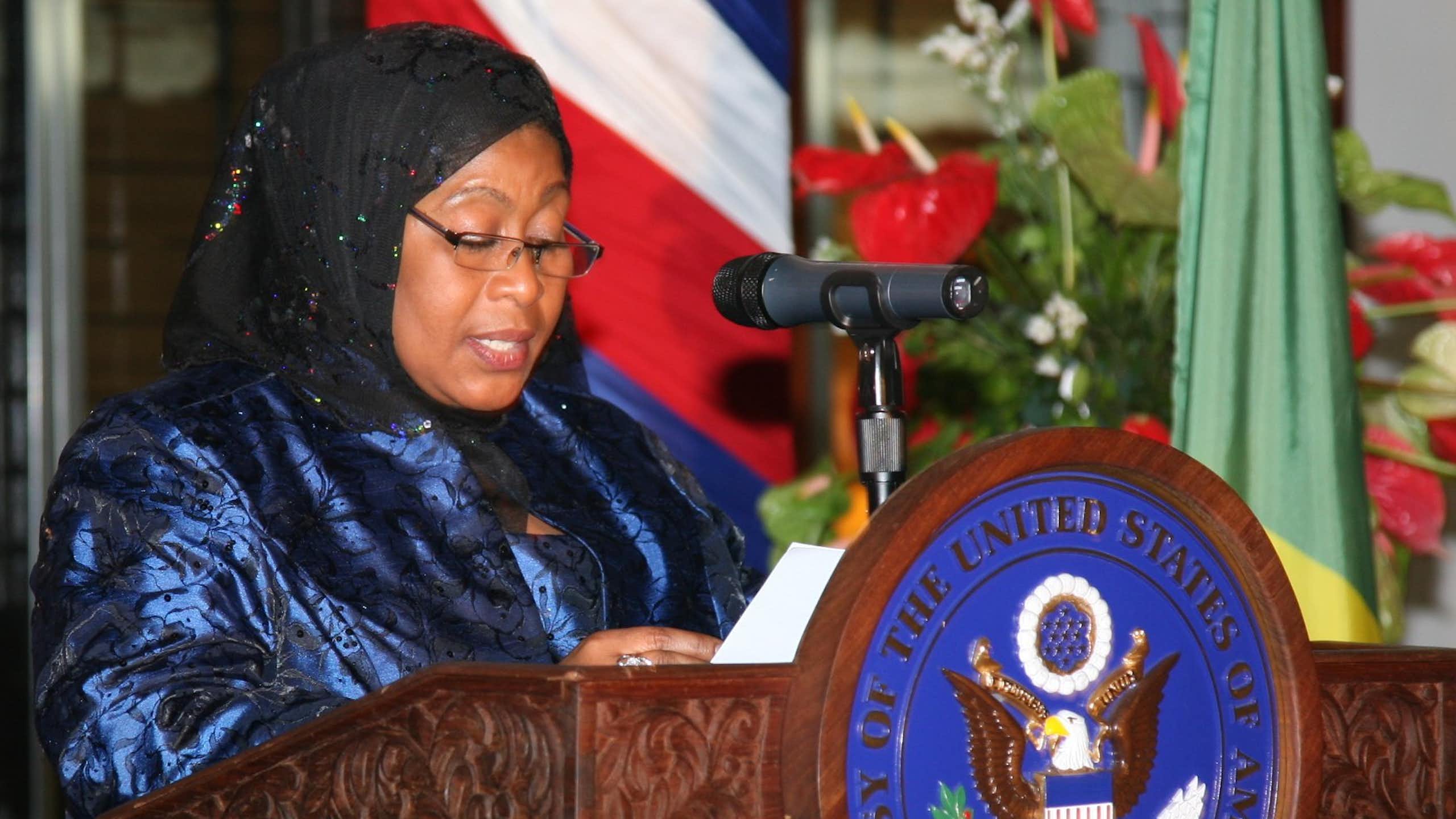 A woman speaking into a microphone placed on a podium written Embassy of the United States of America