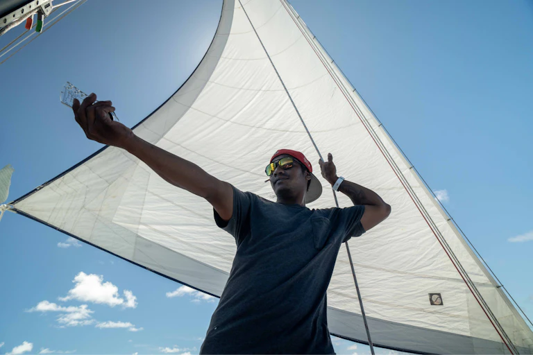 sailor pointing to sea, white sail, blue sky