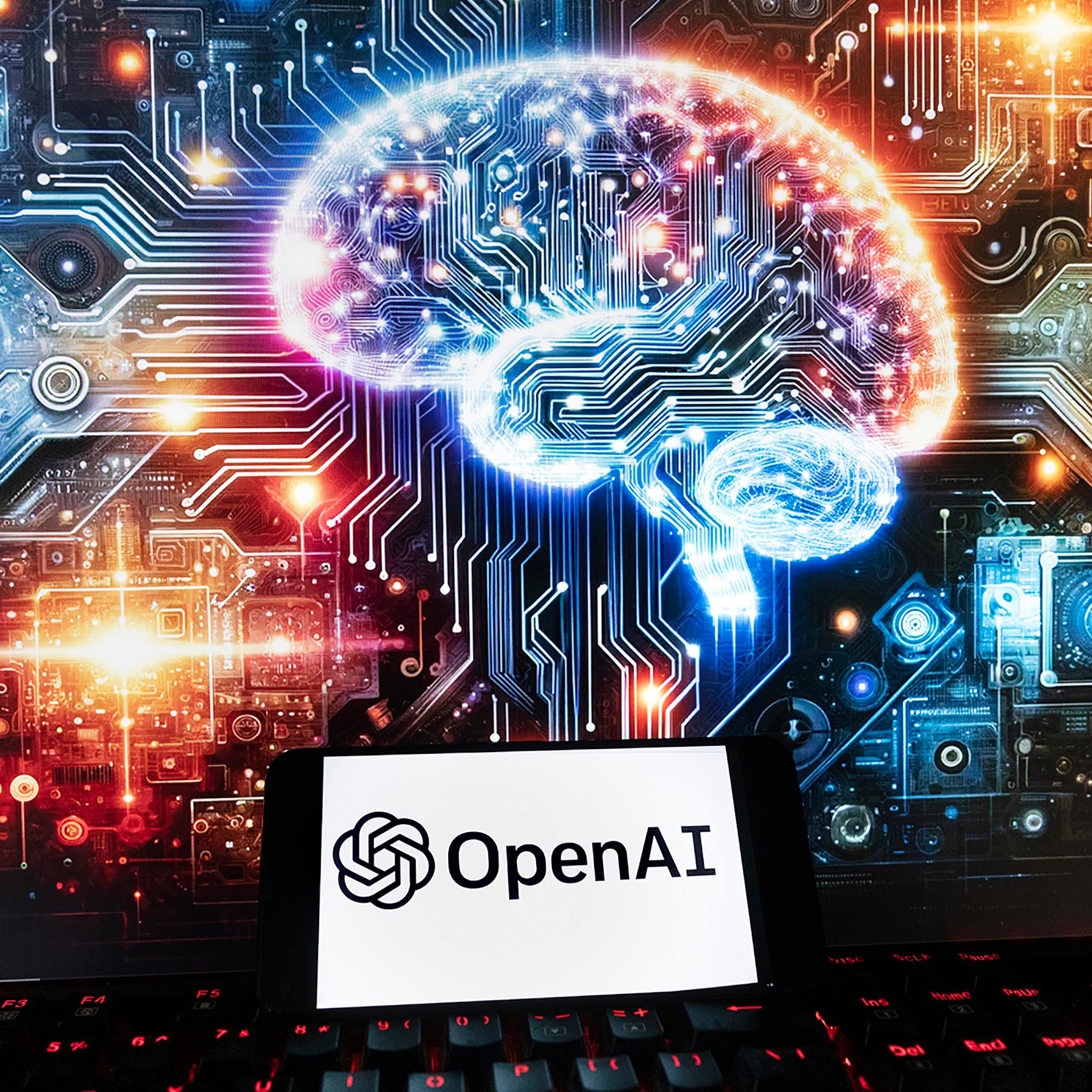 Le logo d’OpenAI est affiché sur un téléphone cellulaire, avec une image sur un écran d’ordinateur représentant un cerveau illuminé et entouré de lumières et de motifs multicolores.