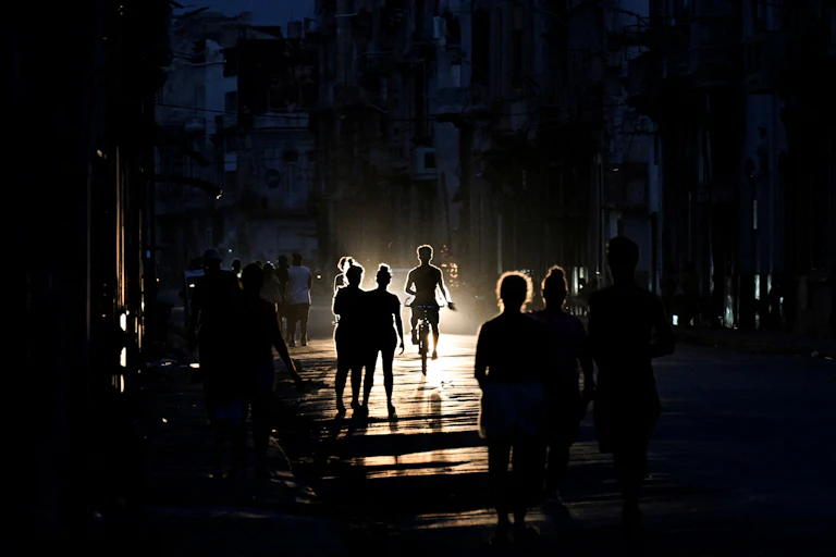 The silhouettes of men and women are seen in a dark street.