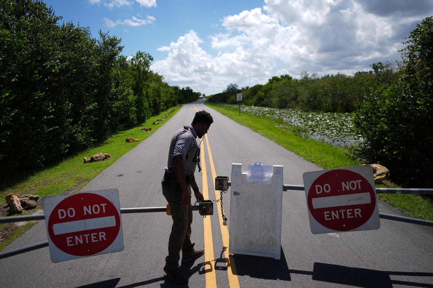 a man in a uniform locks a gate on a road into a park