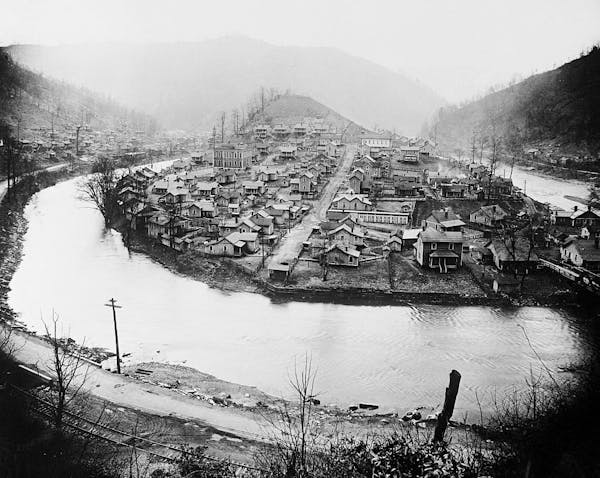 A black and white photo of a settlement on a small hill along a river.