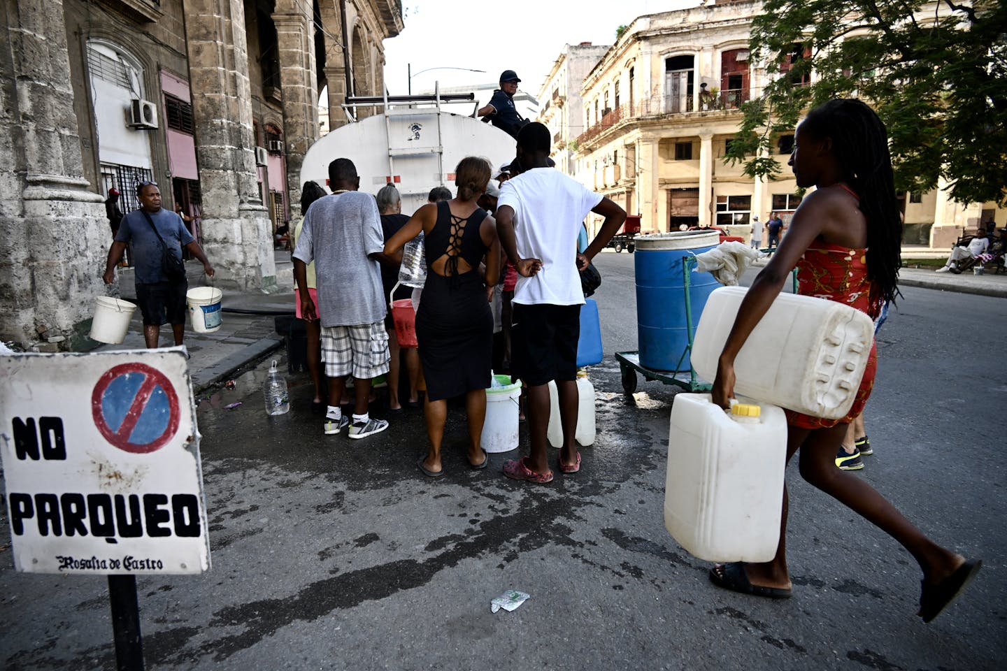 Men and women carrying containers approach a water truck.