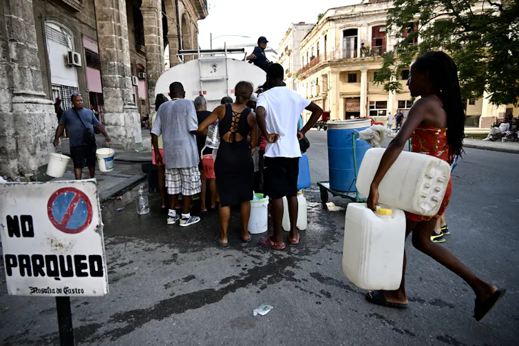 Men and women carrying containers approach a water truck.