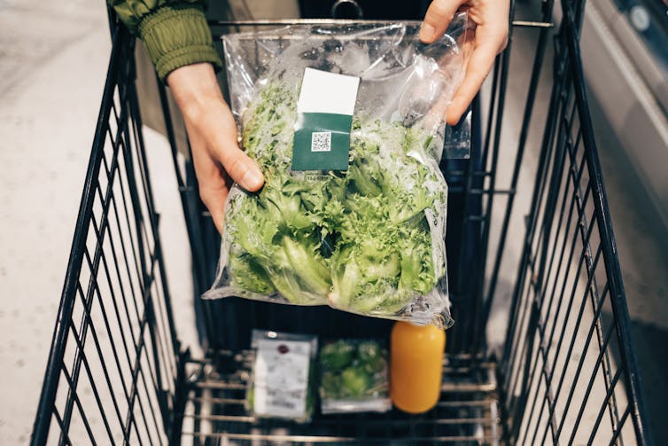 A person's hands hold a packet of lettuce with a scannable label on it.
