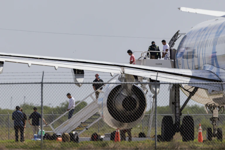 Pessoas algemadas saindo de uma aeronave e descendo uma escada