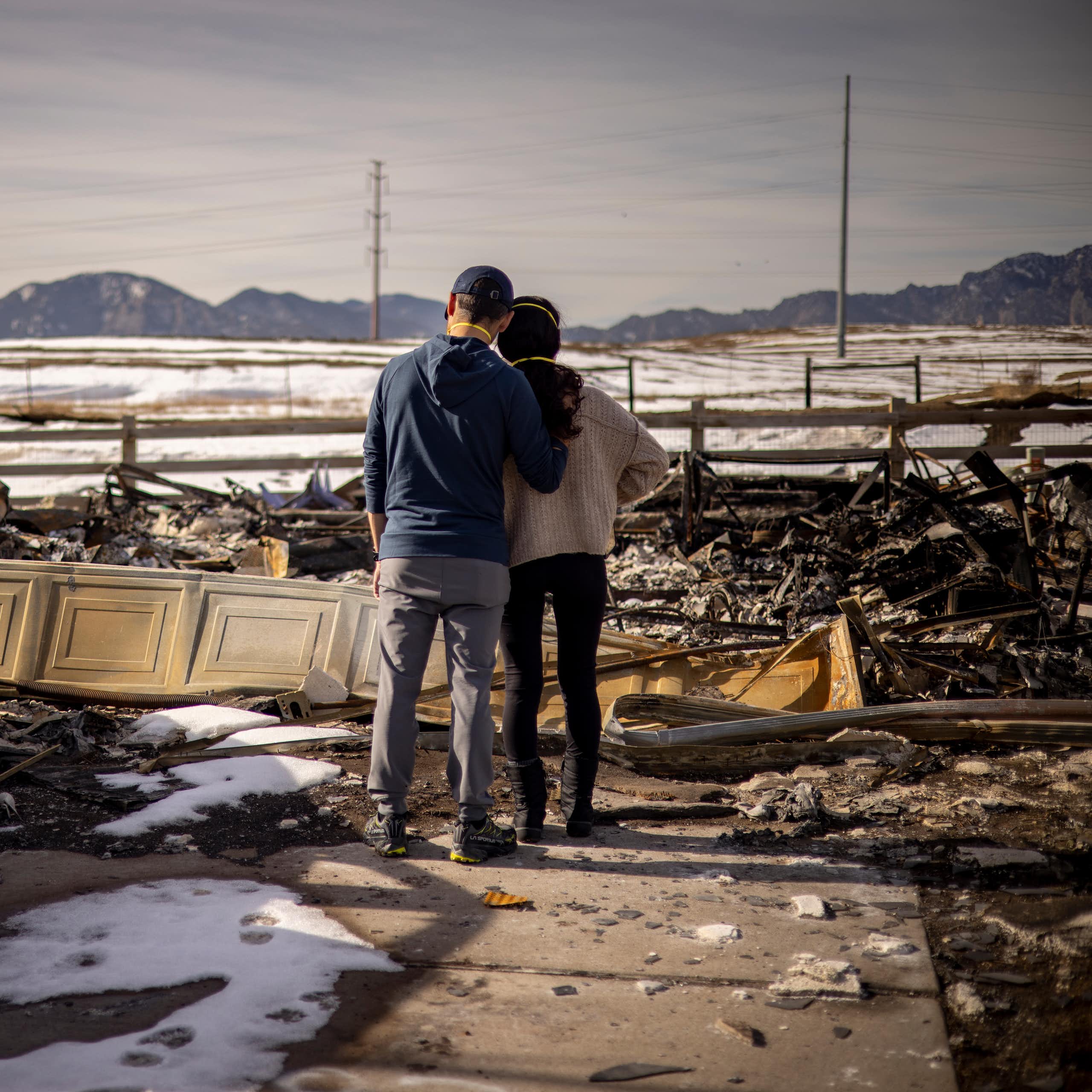 A man and woman stand side-by-side in front of the wreckage of a fire.