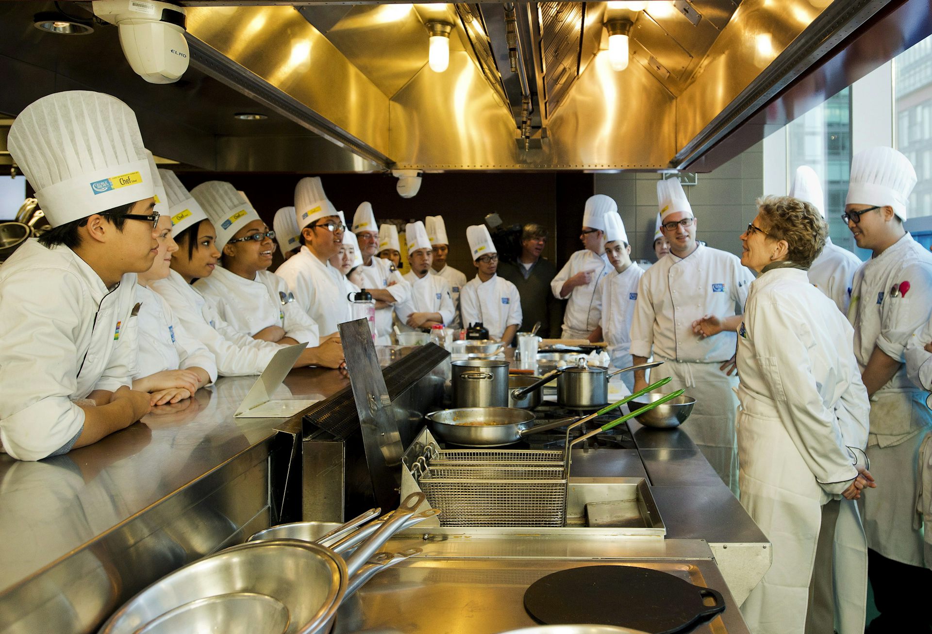 Las personas en las cabezas y blancos fueron vistas alrededor de la cocina con una mujer con trajes y vasos.