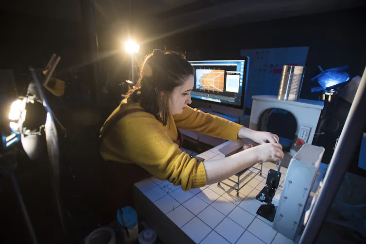A person seen with tech and screen equipment, against a dark room.