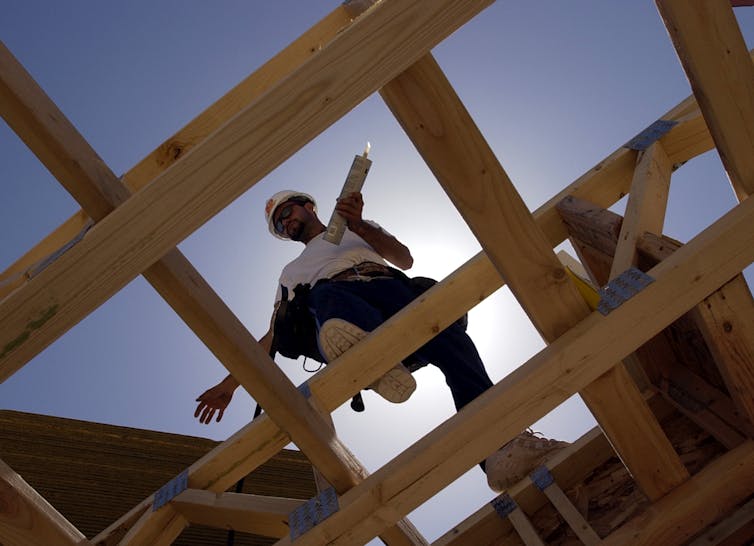 A construction worker walks in the frame of a house.