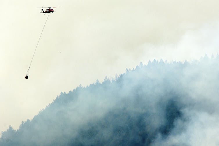 Un helicóptero llevado por el cubo suspendido sobre la carne vuela sobre el humo lleno de humo.